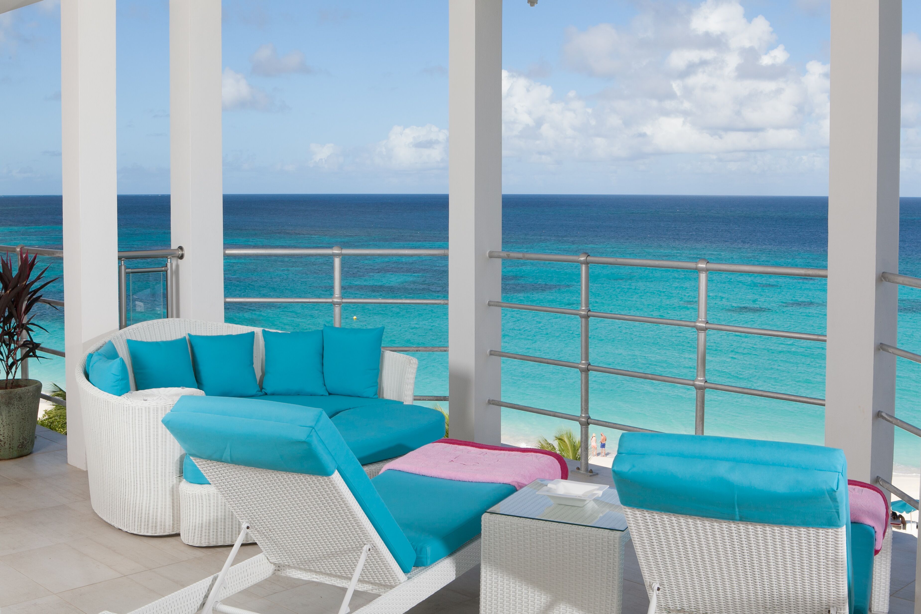 A balcony with a white wicker sofa and chairs, a small table, and a view of the ocean.