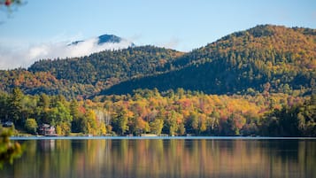 A serene lakeside view with a mountain backdrop, a house by the water, and a clear sky.