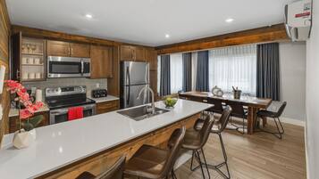A modern kitchen with wooden cabinets, stainless steel appliances, a central island with bar stools, and a dining area with a table and chairs.