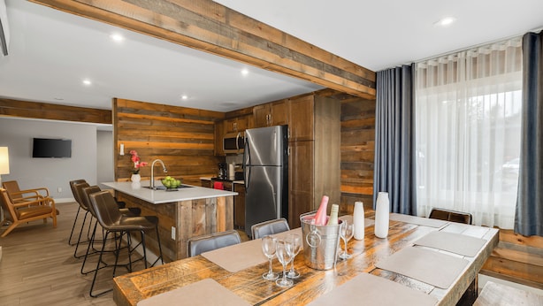 Una cocina moderna con detalles de madera, una zona de comedor con una mesa grande y una barra con taburetes.