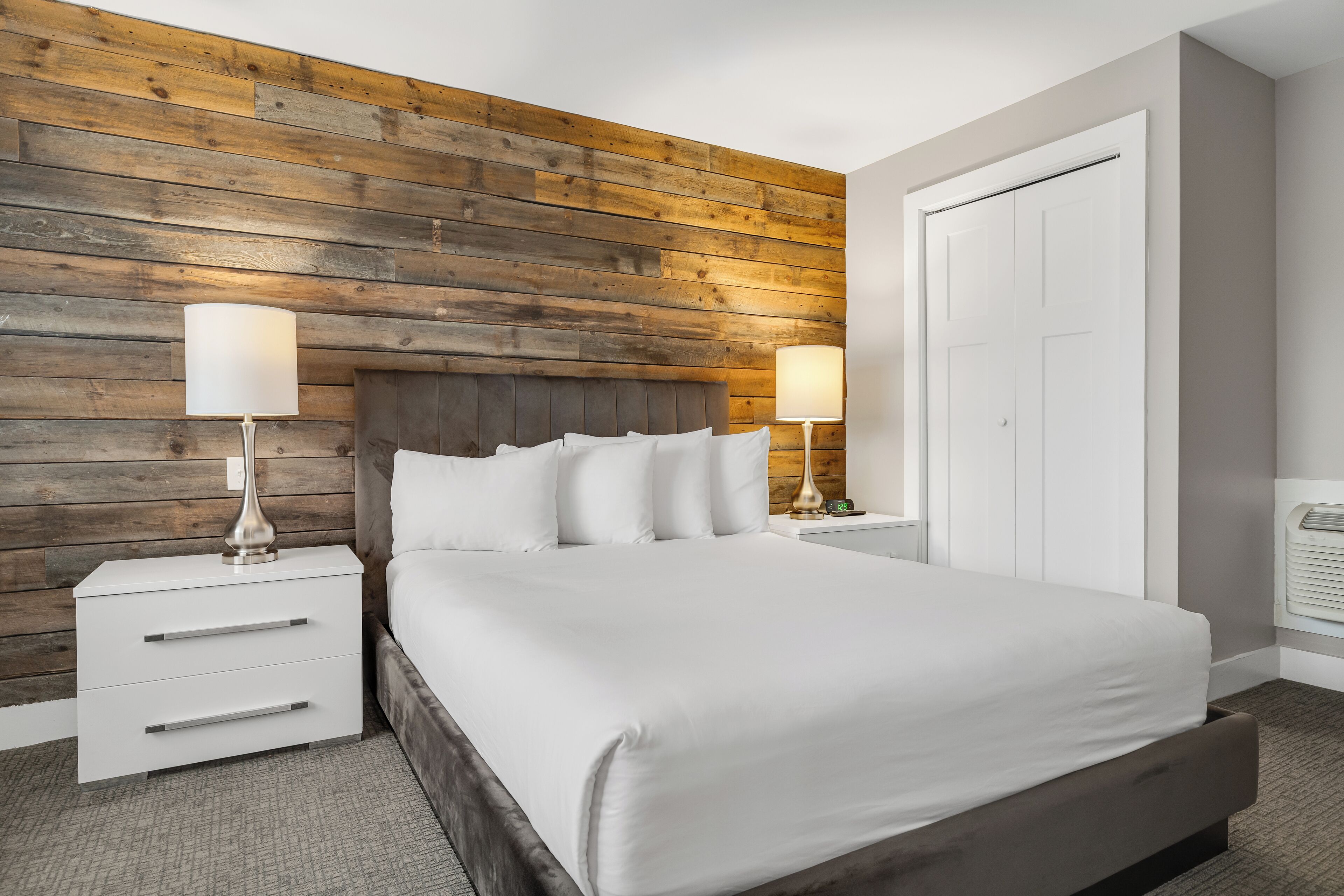 Una cama bien hecha con sábanas blancas, cabecera de madera y dos lámparas de noche.