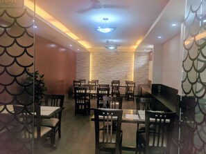 A restaurant with a modern interior, featuring wooden tables and chairs, a stone wall, and recessed ceiling lighting. - Hotel Windsor Castle (Gurugram)