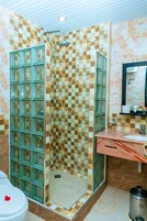 Casa de banho com parede de azulejos xadrez, cabine de duche em vidro, lavatório de mármore e sanita com um objeto vermelho em cima.