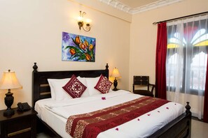 A neatly made bed with white linens and red accents, a painting above the bed, and two bedside lamps.