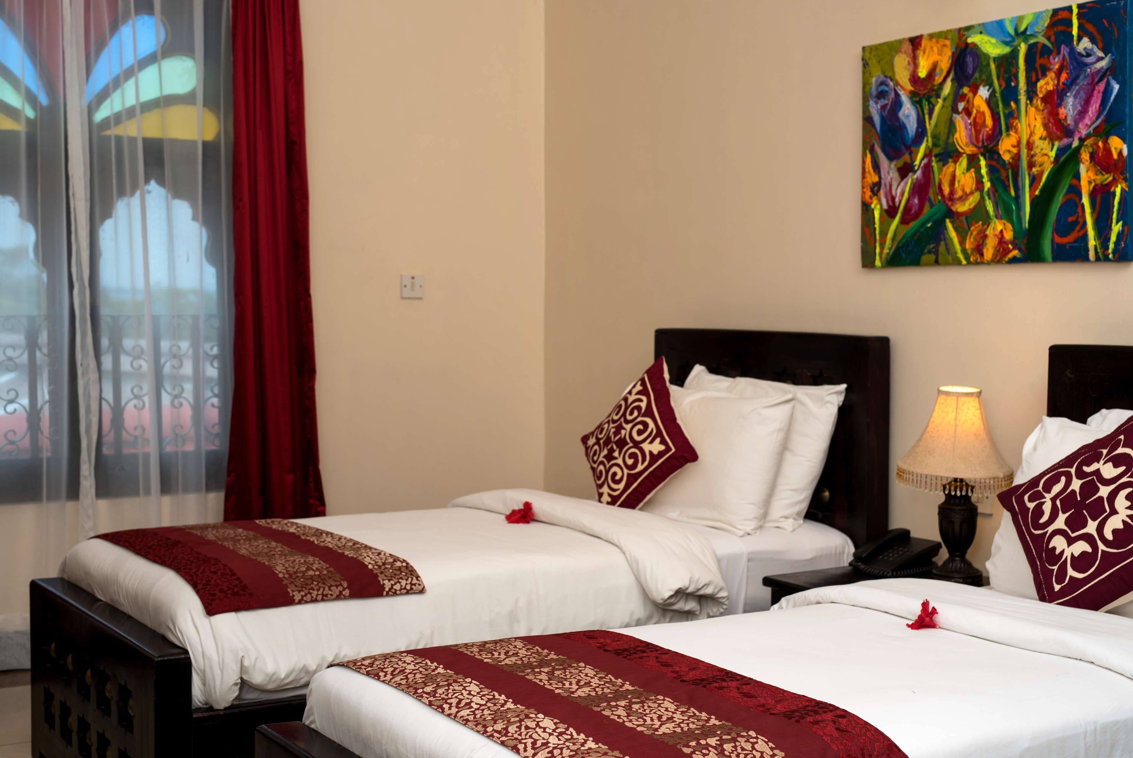 A hotel room with two beds, a nightstand with a lamp, and a colorful painting on the wall.