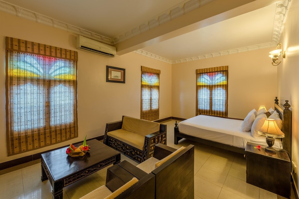 Une chambre d’hôtel comprenant un canapé, un lit, une table de chevet avec une lampe et une petite table ornée d’un objet décoratif.