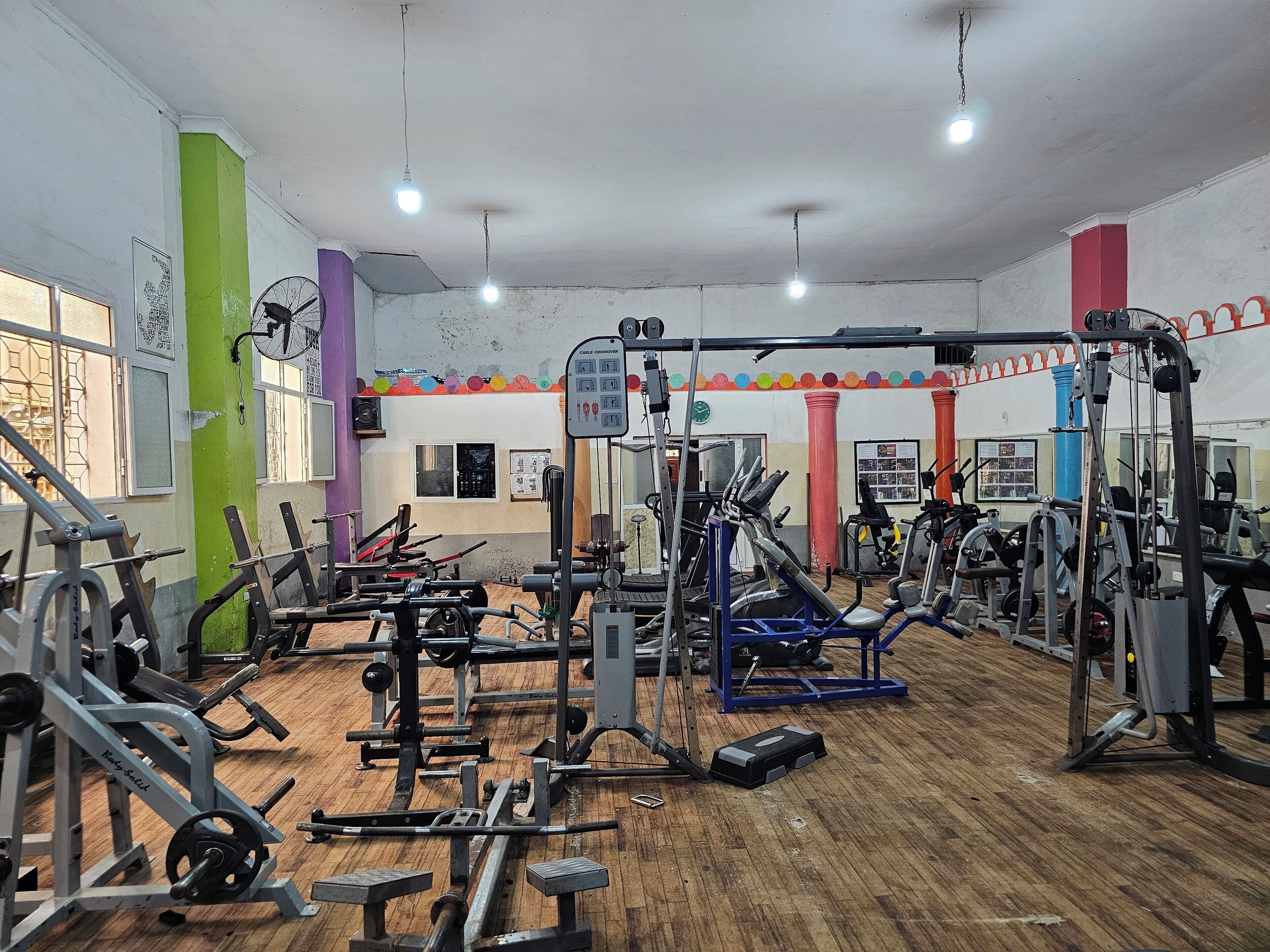 Un gimnasio con diverso equipamiento de ejercicio, suelo de madera y decoraciones de pared coloridas.
