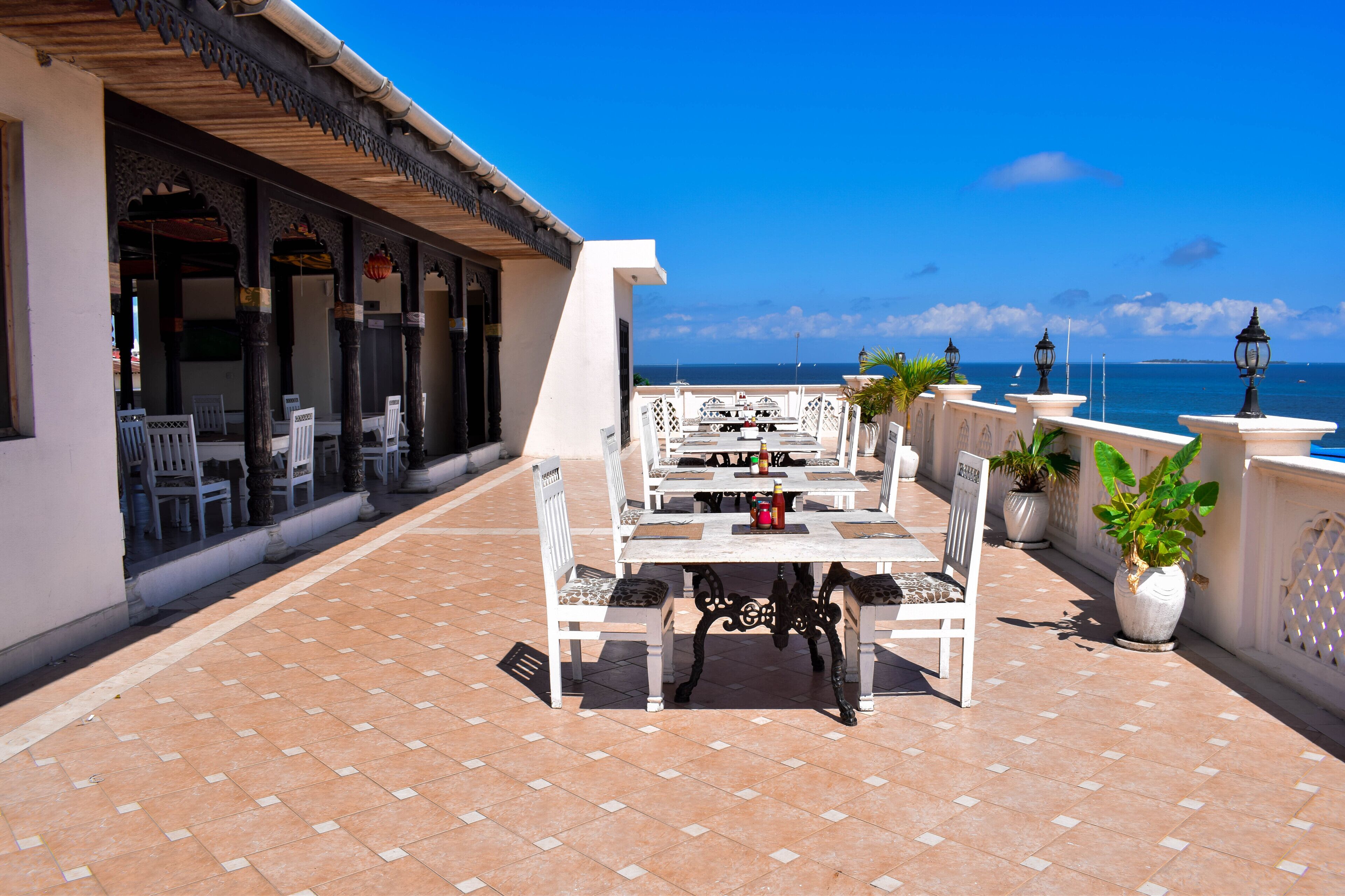 An outdoor patio with white furniture, a tiled floor, and a view of the ocean.