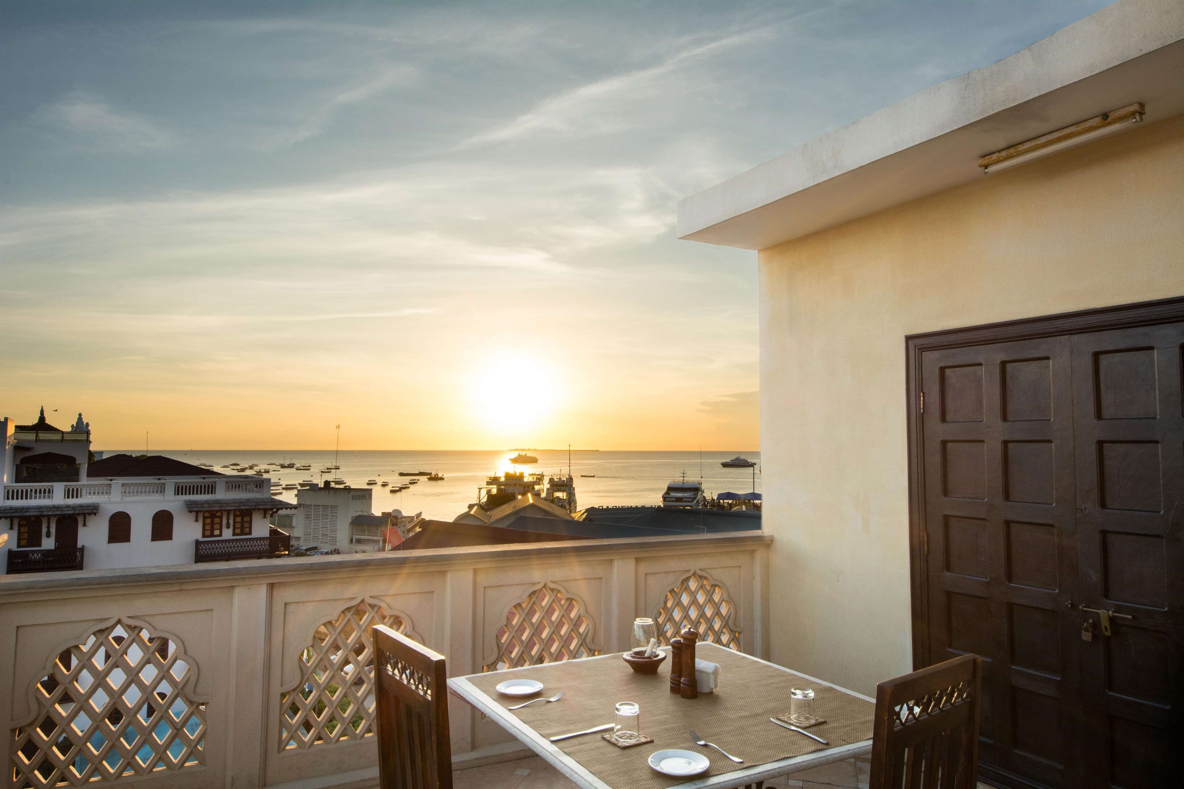 A balcony with a table set for dining, overlooking a coastal view with boats and buildings.