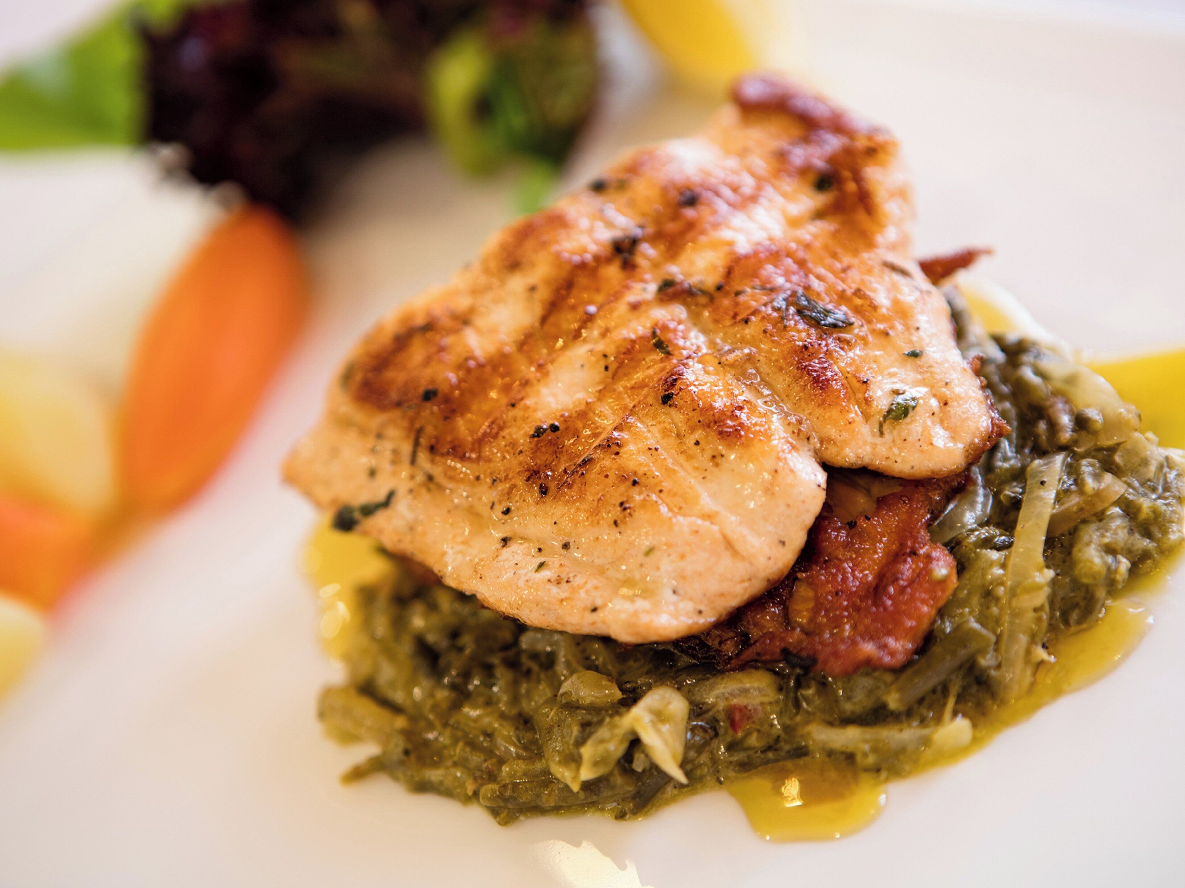 A plate with a piece of grilled chicken, greens, and a slice of tomato.