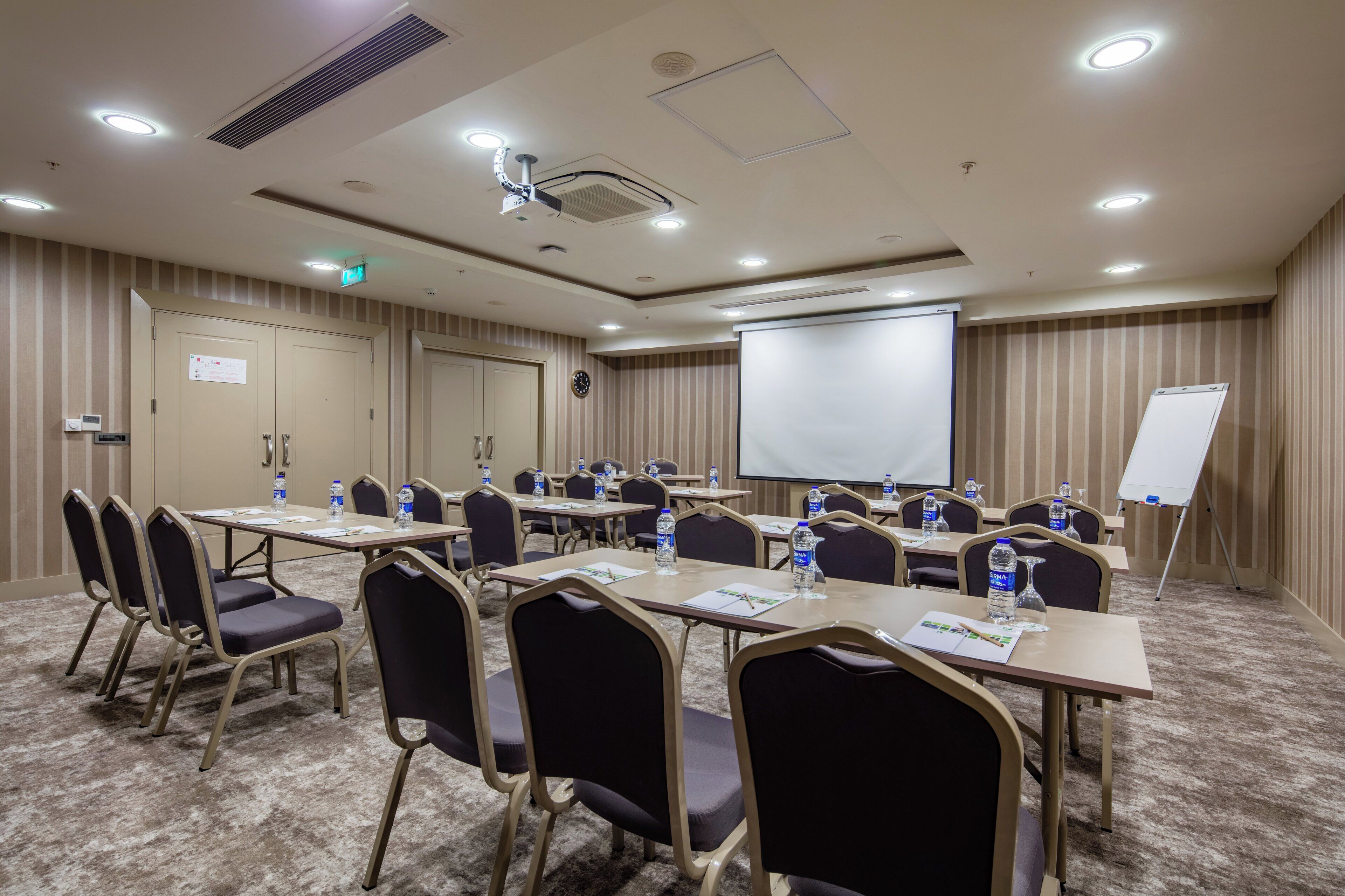 A conference room with tables, chairs, a projector screen, and a whiteboard.
