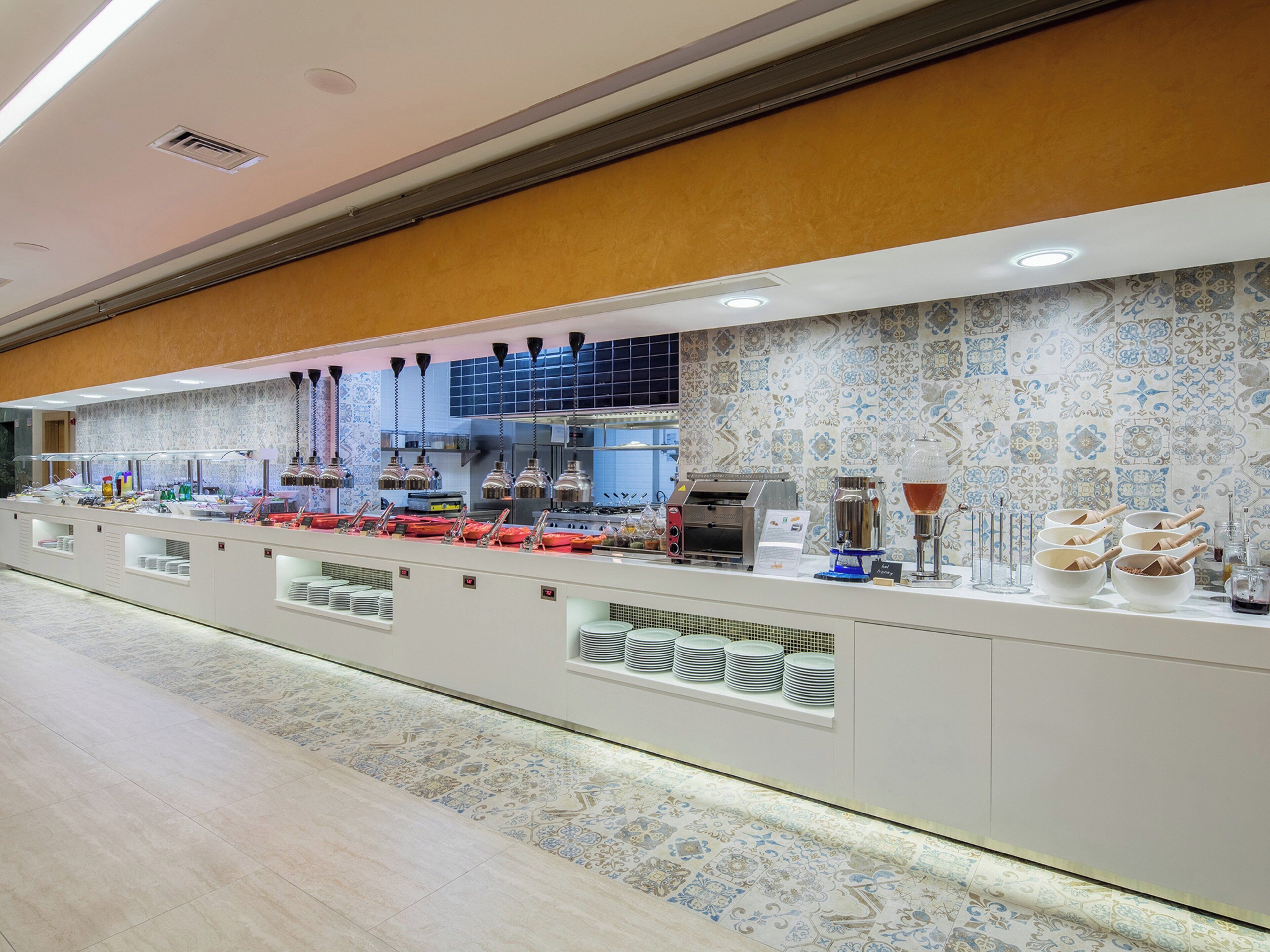 A buffet setup with various food items and utensils, a coffee machine, and a patterned wall.