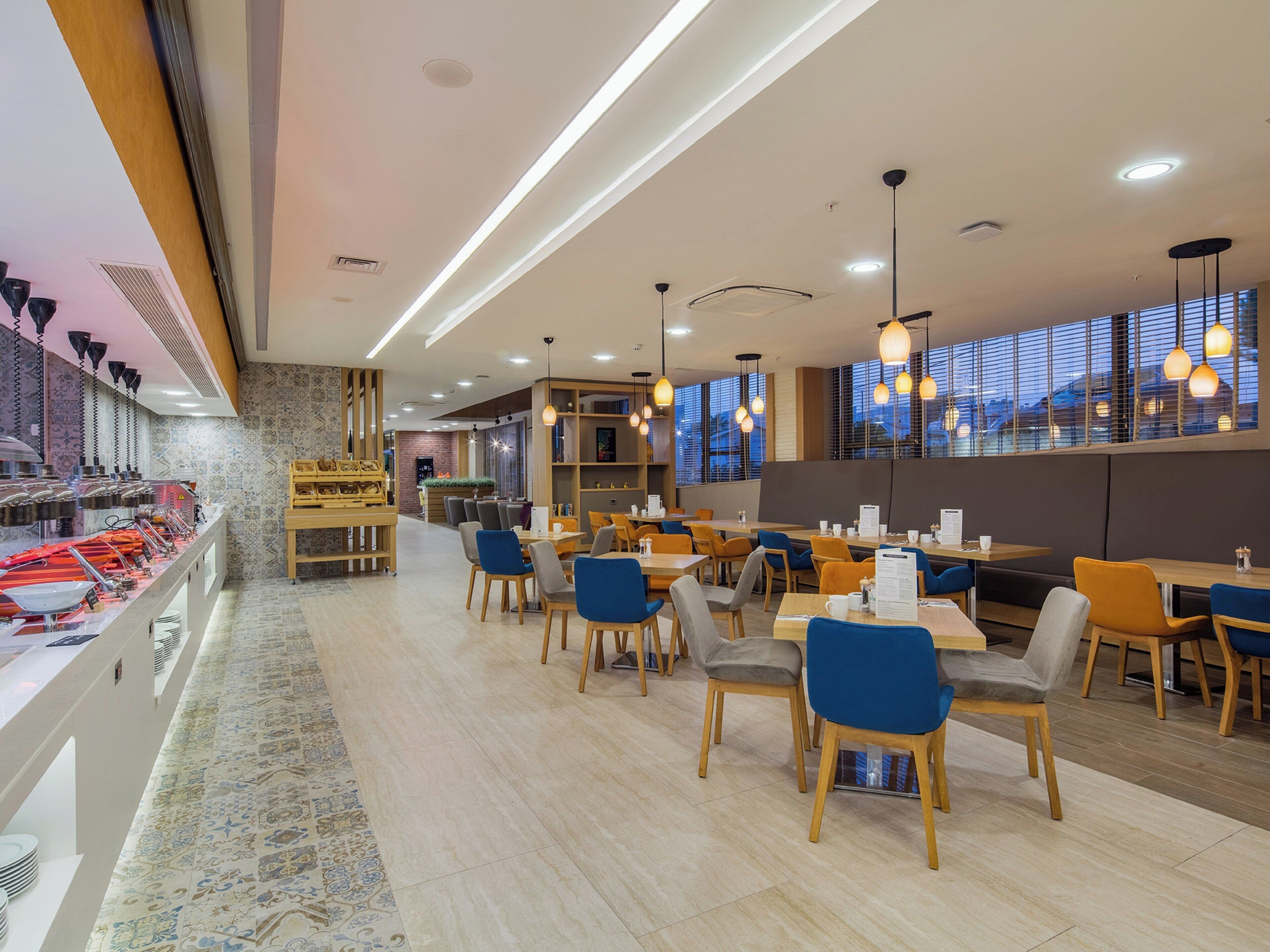 A modern restaurant interior with a long counter, multiple dining tables, and chairs.