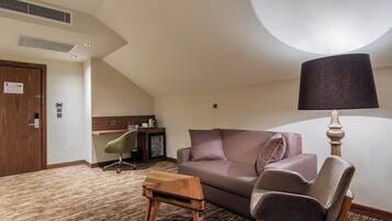 Ein Hotelzimmer mit einer Couch, einem kleinen Tisch, einer Lampe, einem Sessel, einem Schreibtisch und einem Kühlschrank.