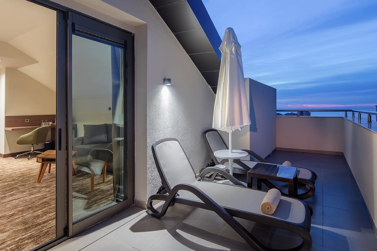 A modern balcony with a glass door leading to a living area, furnished with a sofa, chairs, and a small table.
