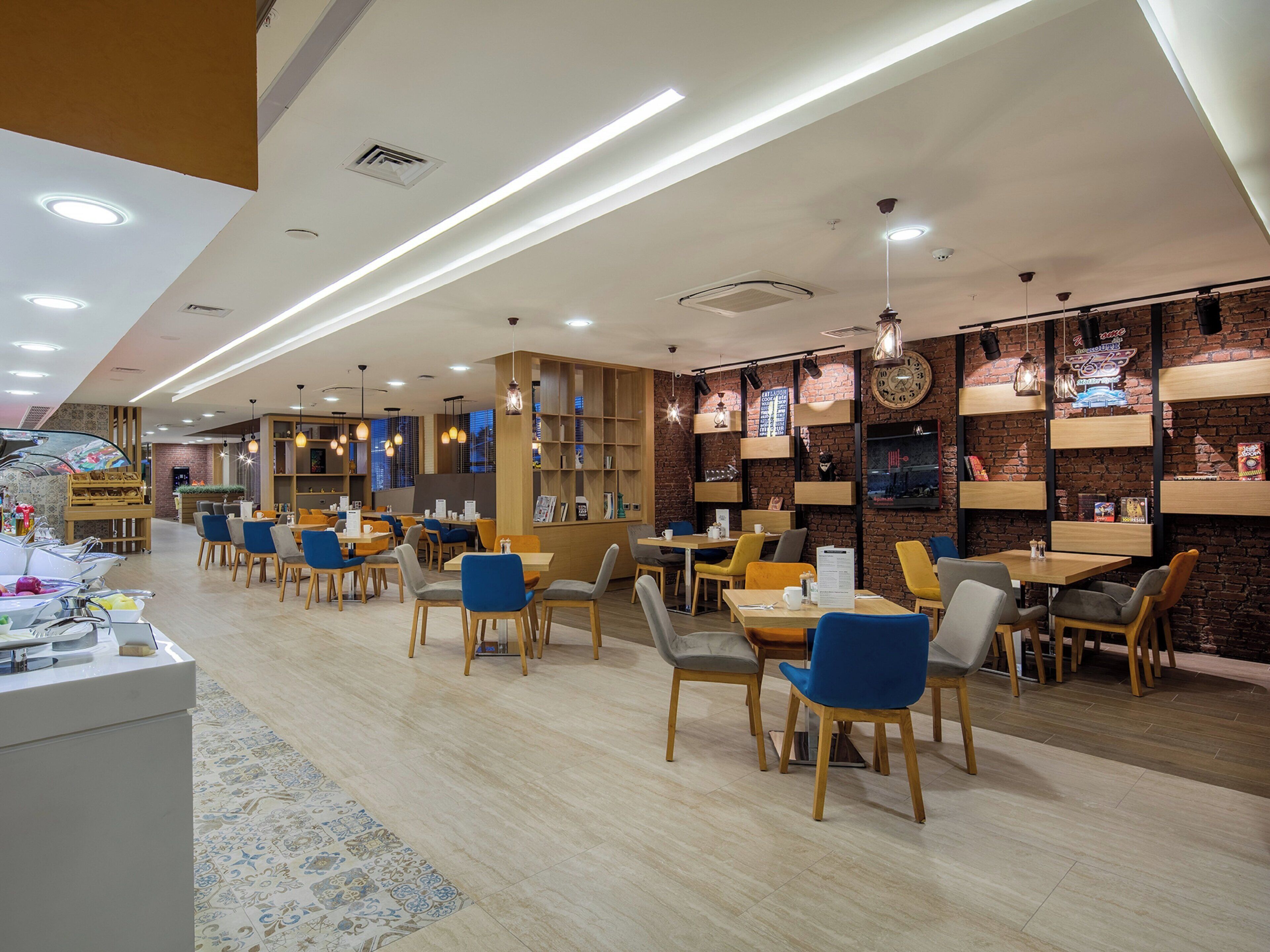 Un café moderno con mesas y sillas de madera, un piano y una pared de ladrillo con estanterías.