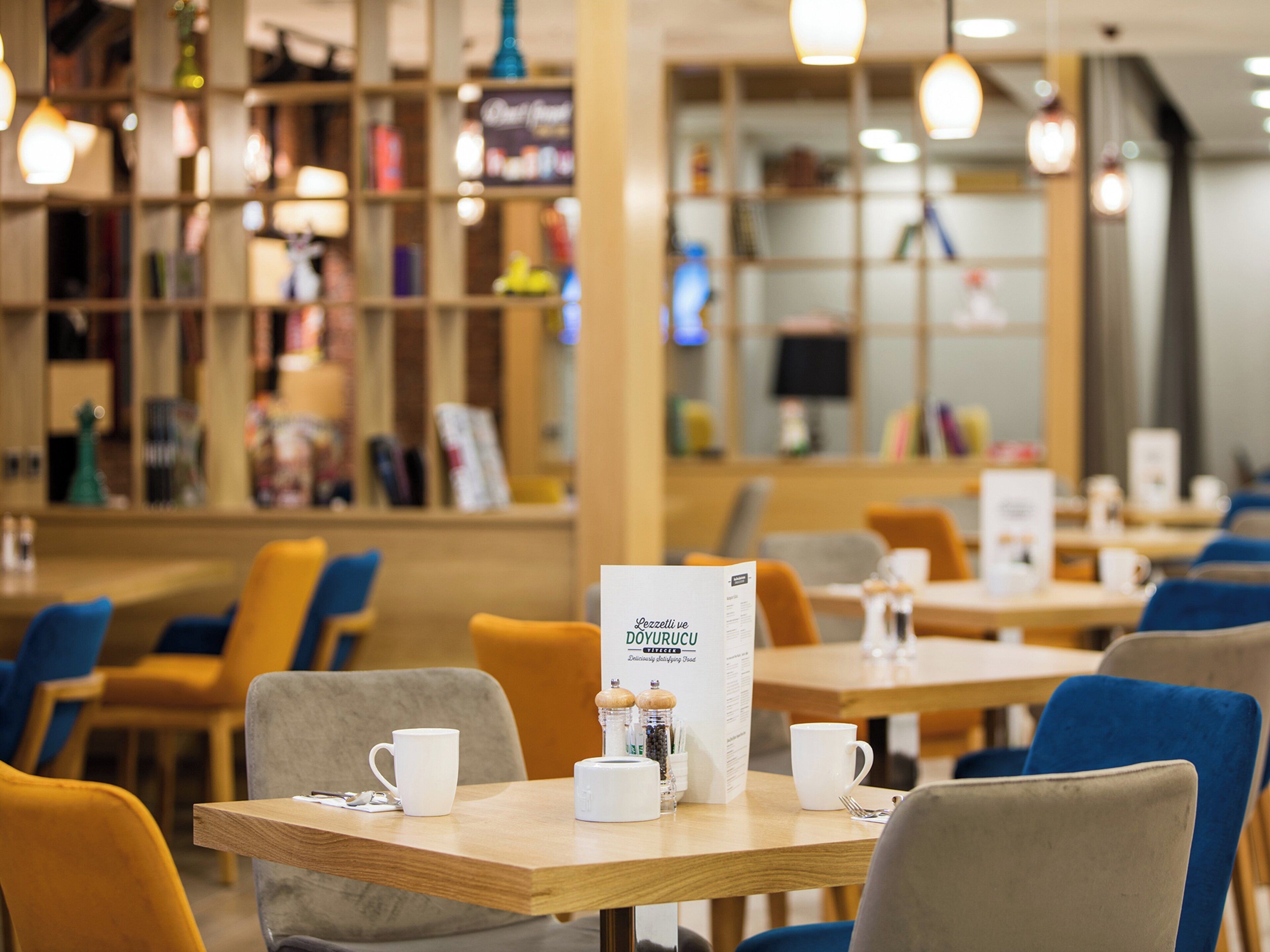 A café with tables and chairs, a menu stand, and shelves with various items.