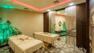 A spa room with two massage tables, a mirror, a sink, and a decorative wall with vertical elements.