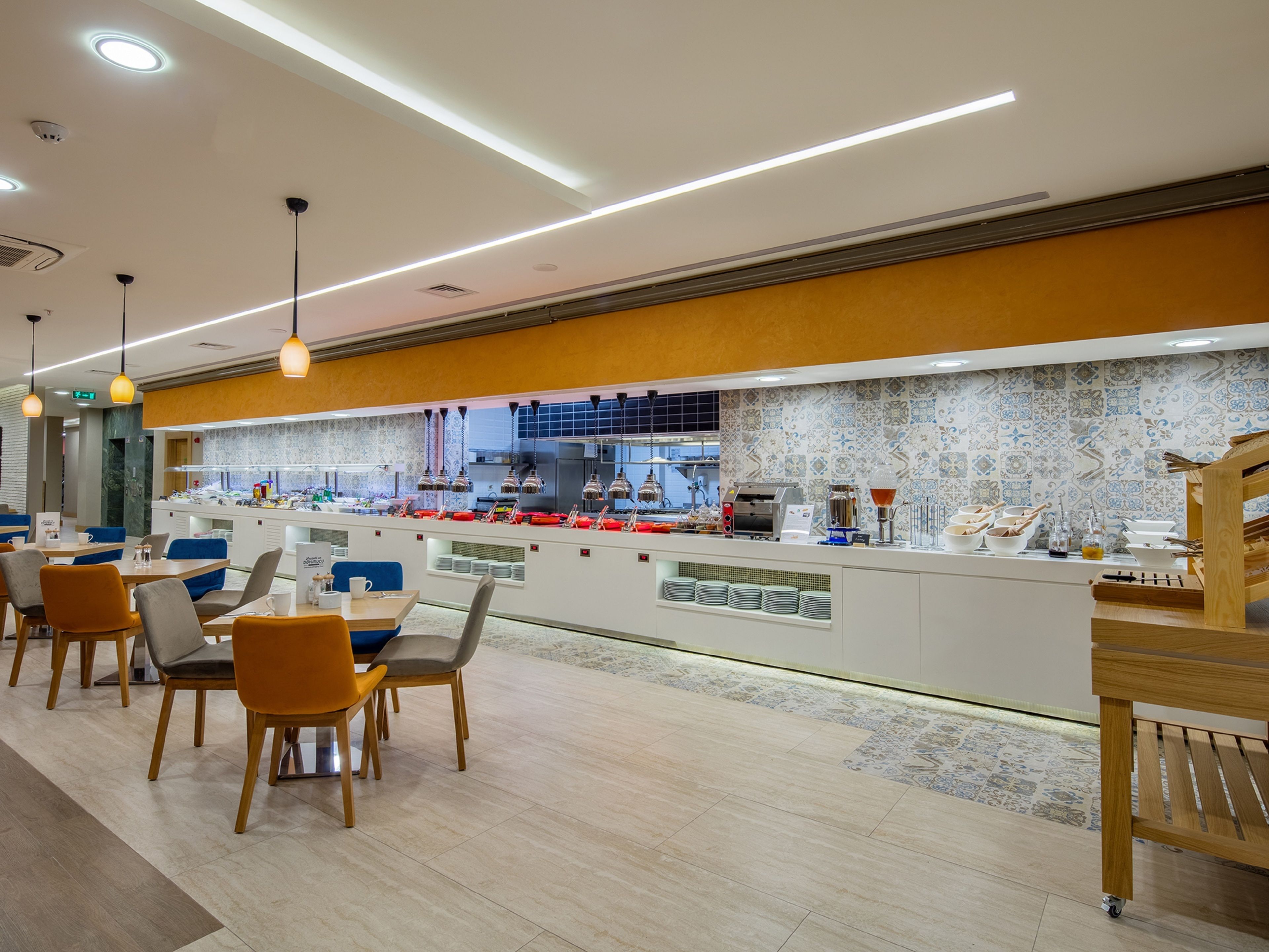 Een modern café met een lange balie, een zithoek met tafels en stoelen, en een keuken op de achtergrond.