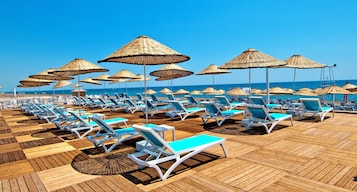 Un espace de détente aménagé sur la plage, avec des rangées de chaises longues et des parasols en feuilles de palmier.