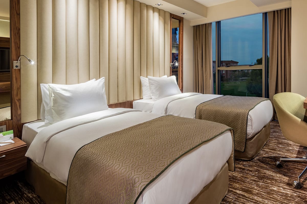 A hotel room with two beds, a desk, a chair, and a large window with a view.