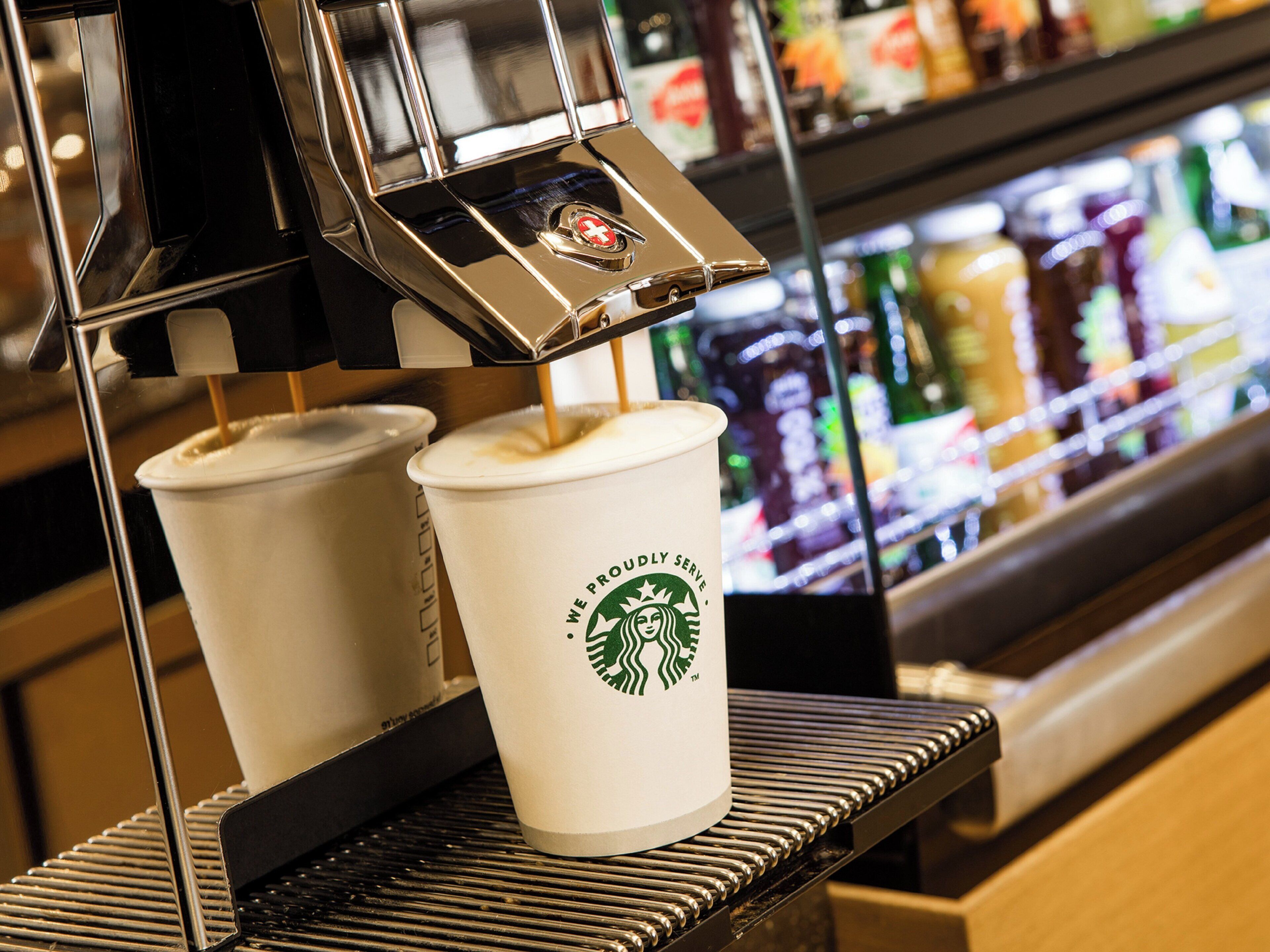 A coffee machine dispensing coffee into two Starbucks cups.