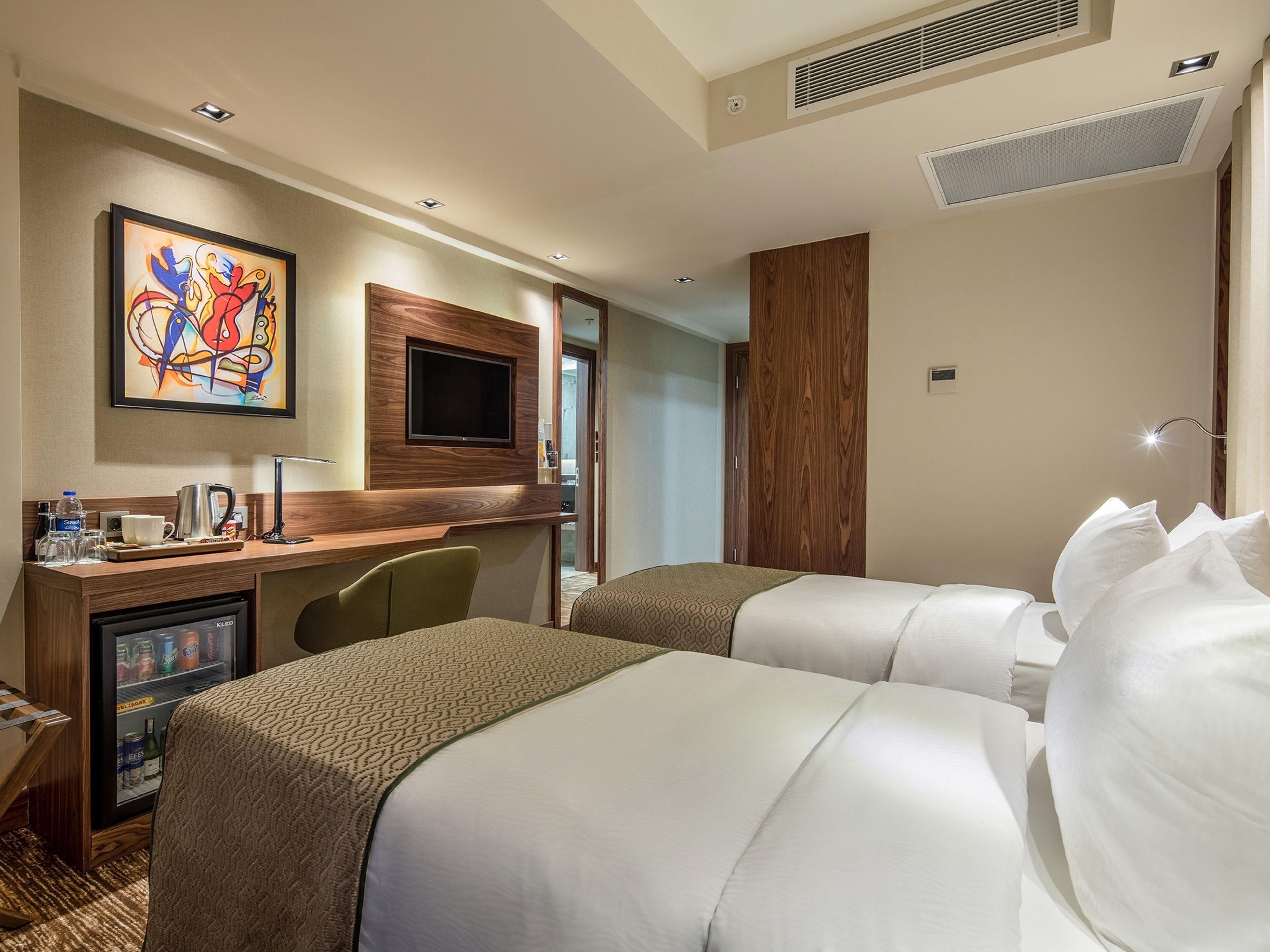 A hotel room with two beds, a desk with a coffee maker, a TV, and a minibar.