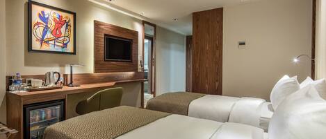 A hotel room with two beds, a desk with a coffee maker, a TV, and a minibar.