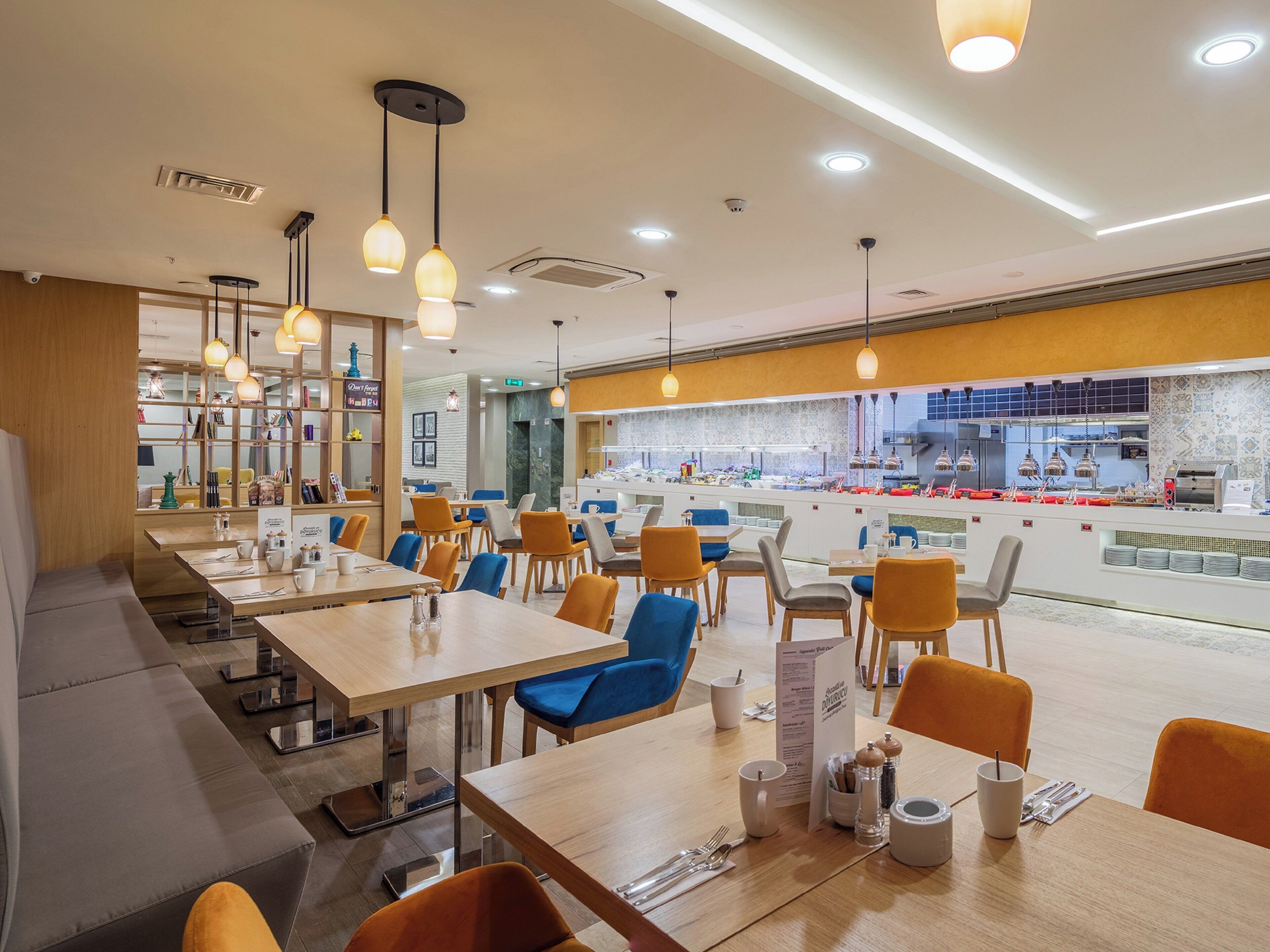 A modern restaurant with multiple dining tables, chairs, and a visible kitchen area.