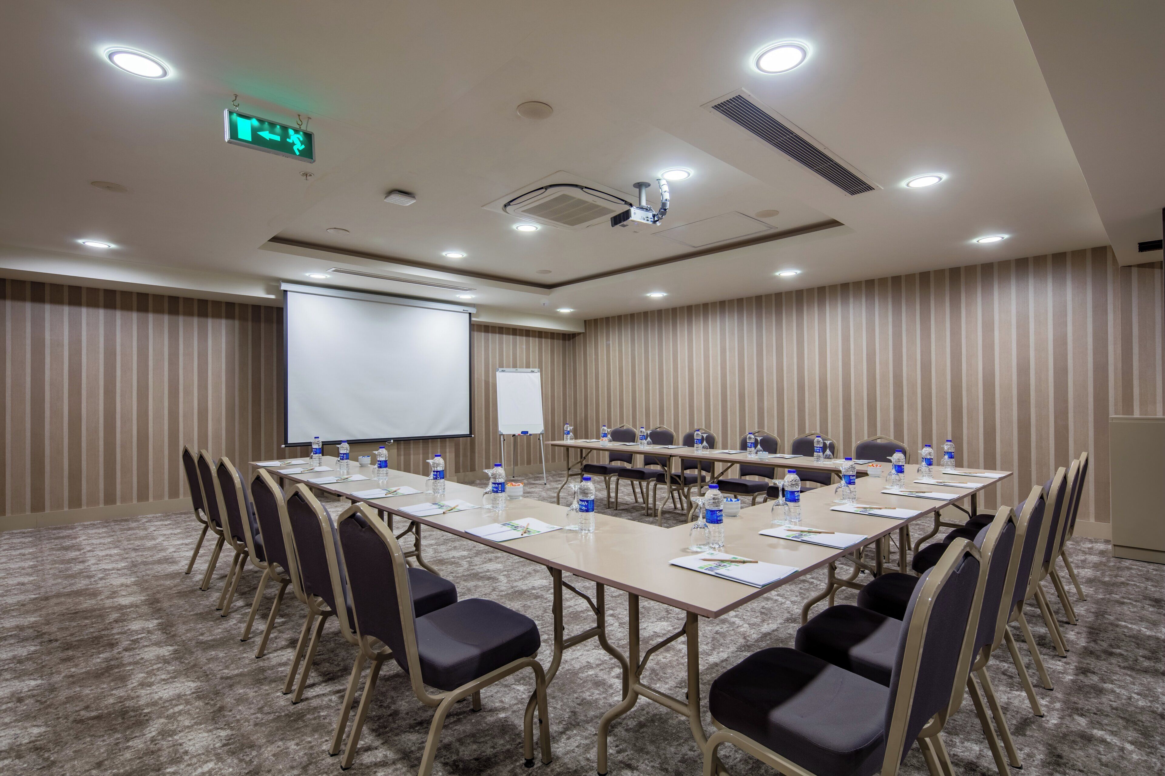 Una sala de conferencias con una gran mesa, sillas, una pantalla para proyector y una pizarra.