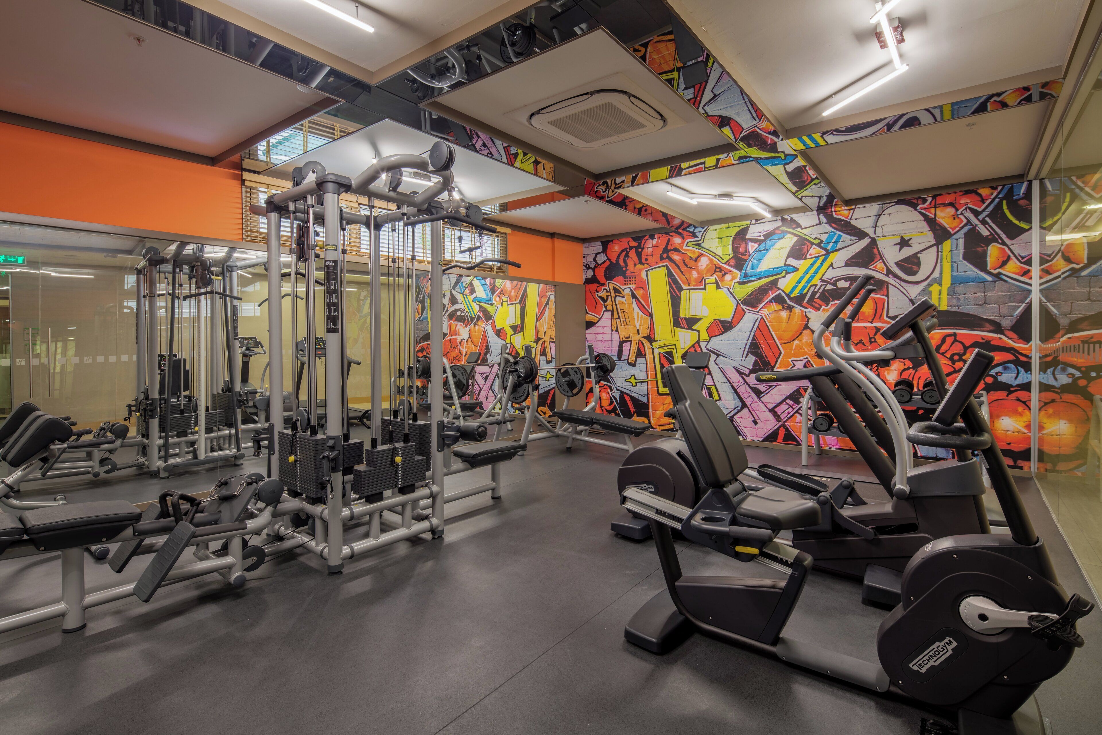 Een sportschool met diverse fitnessapparaten, een vrolijke graffiti muur en een spiegelend plafond.