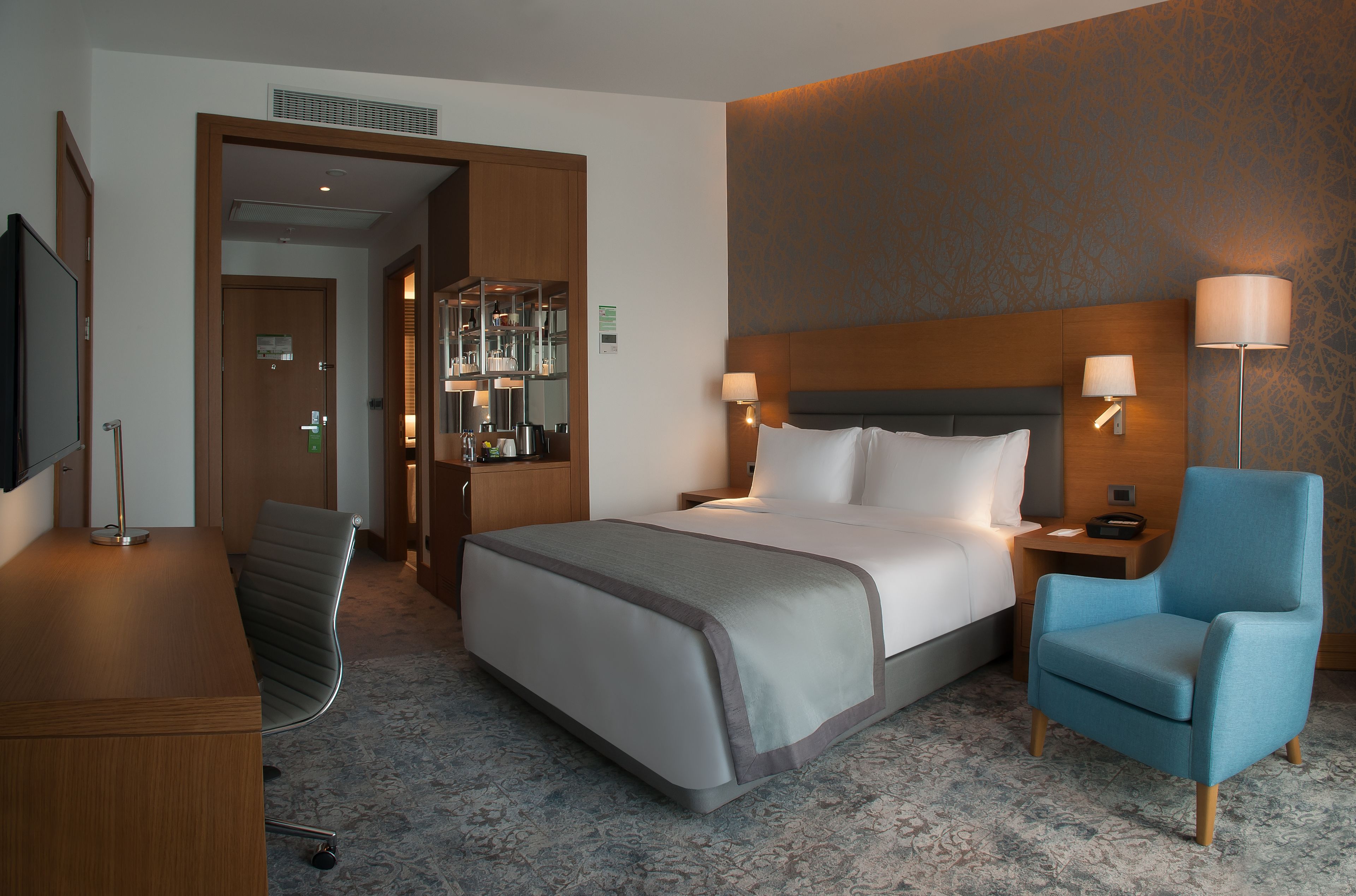 A hotel room with a bed, a desk, a chair, and a television.