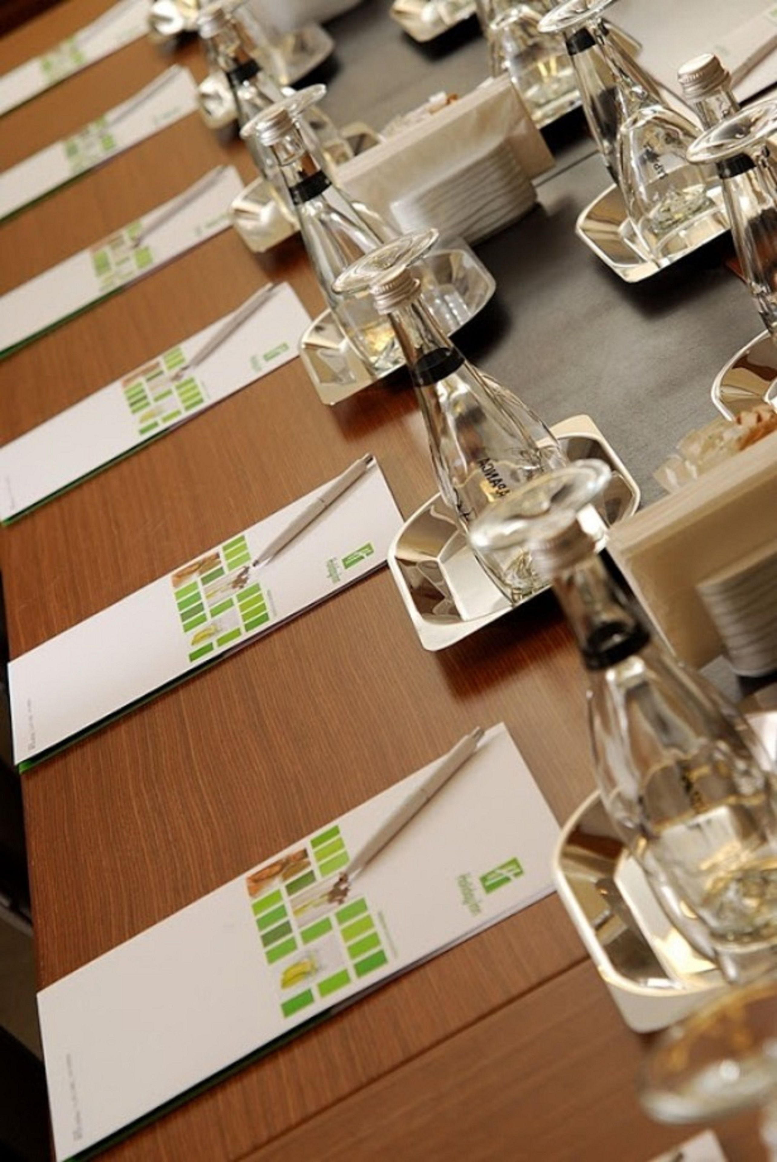 Varias mesas con botellas de vidrio transparente y manteles individuales blancos con diseños en verde y amarillo.