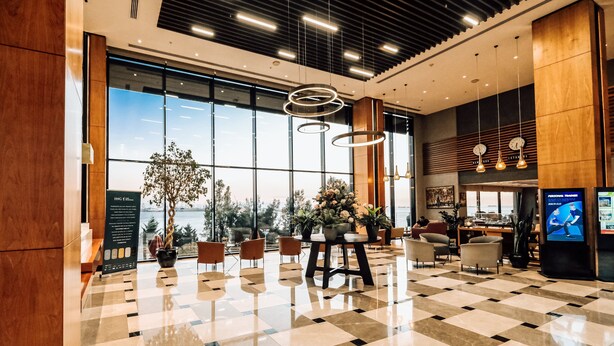 Un hall amplio con piso a cuadros, ventanas grandes y lámparas modernas.