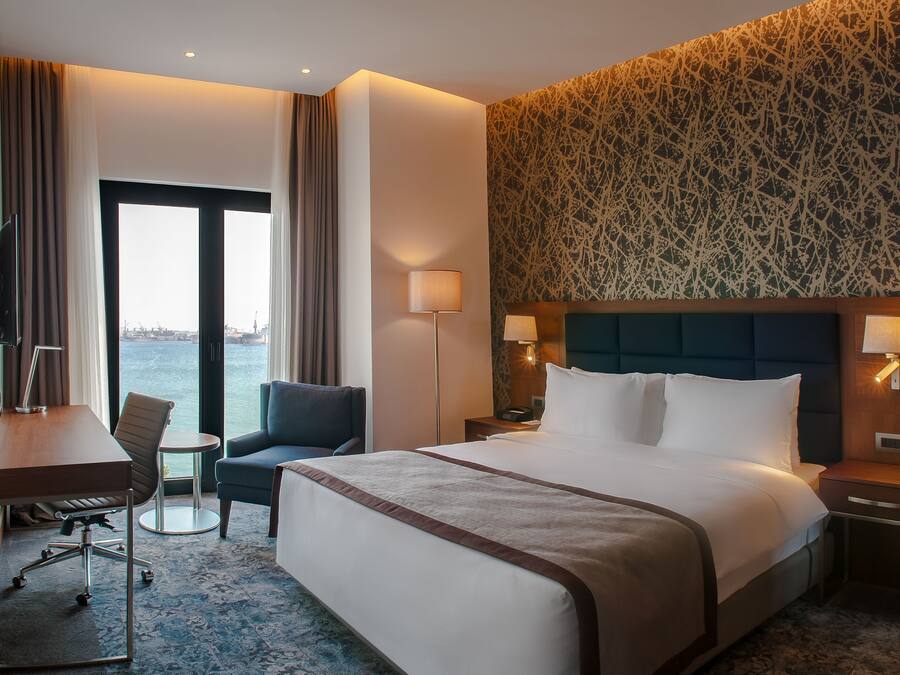 Habitación de hotel con una cama grande, un escritorio, una silla, una mesita y vistas al agua.
