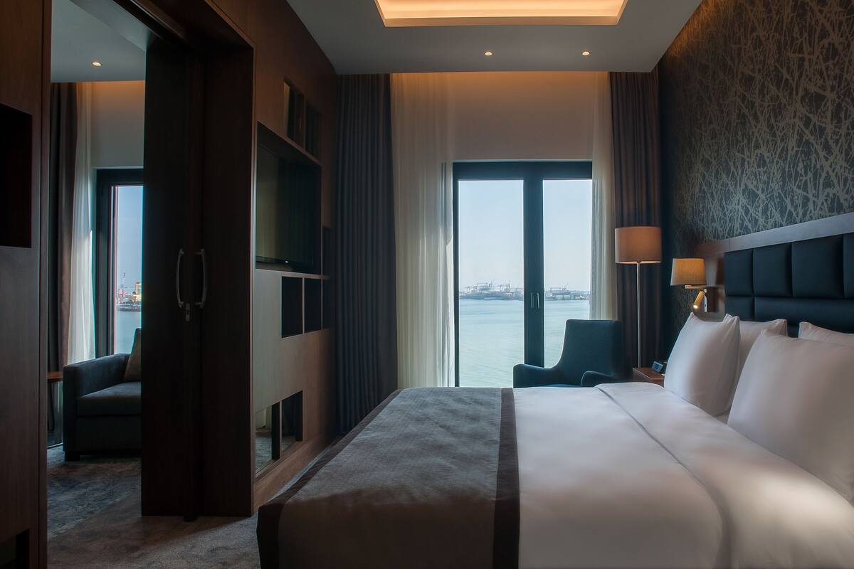 A hotel room with a large bed, a TV, a desk, and a view of the water.