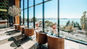 Un espacio interior moderno con ventanas amplias, una planta en maceta y arreglos de asientos.