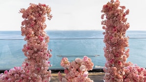 Una terraza con un arco floral y vista al mar.