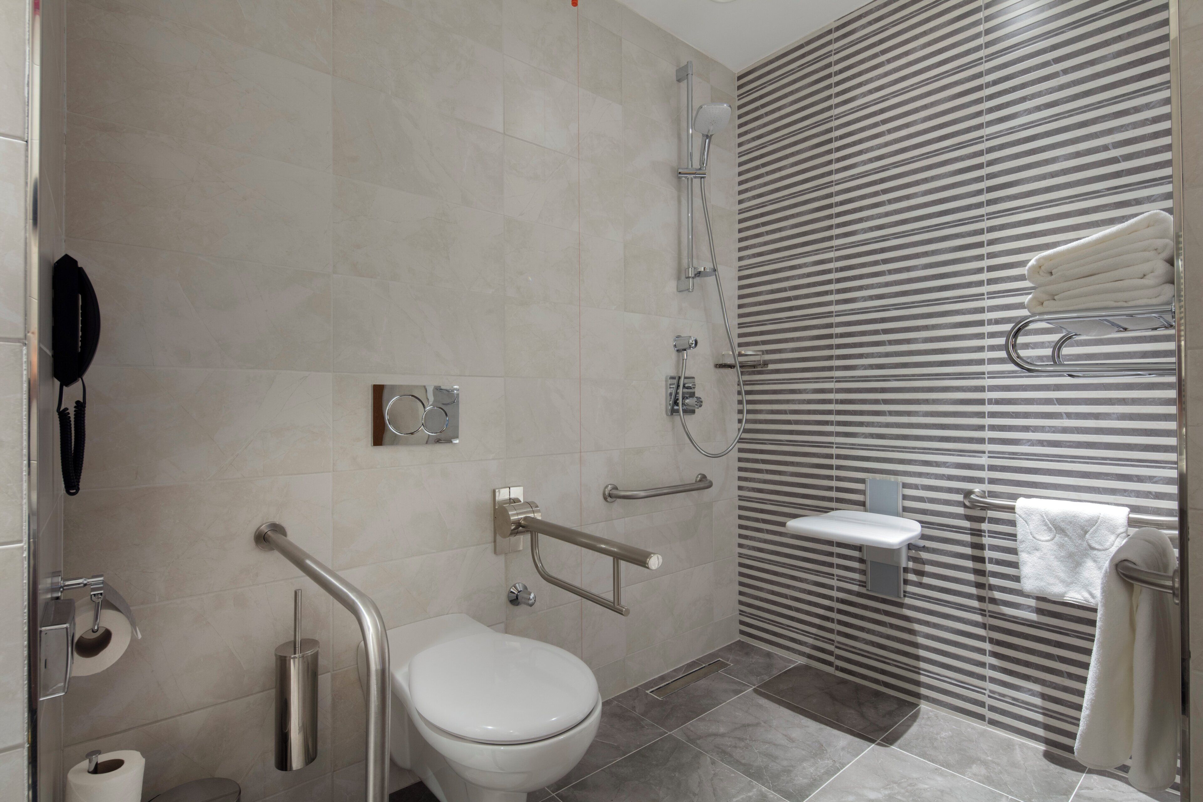 Un baño moderno con inodoro, barras de apoyo, ducha y perchero para toallas.