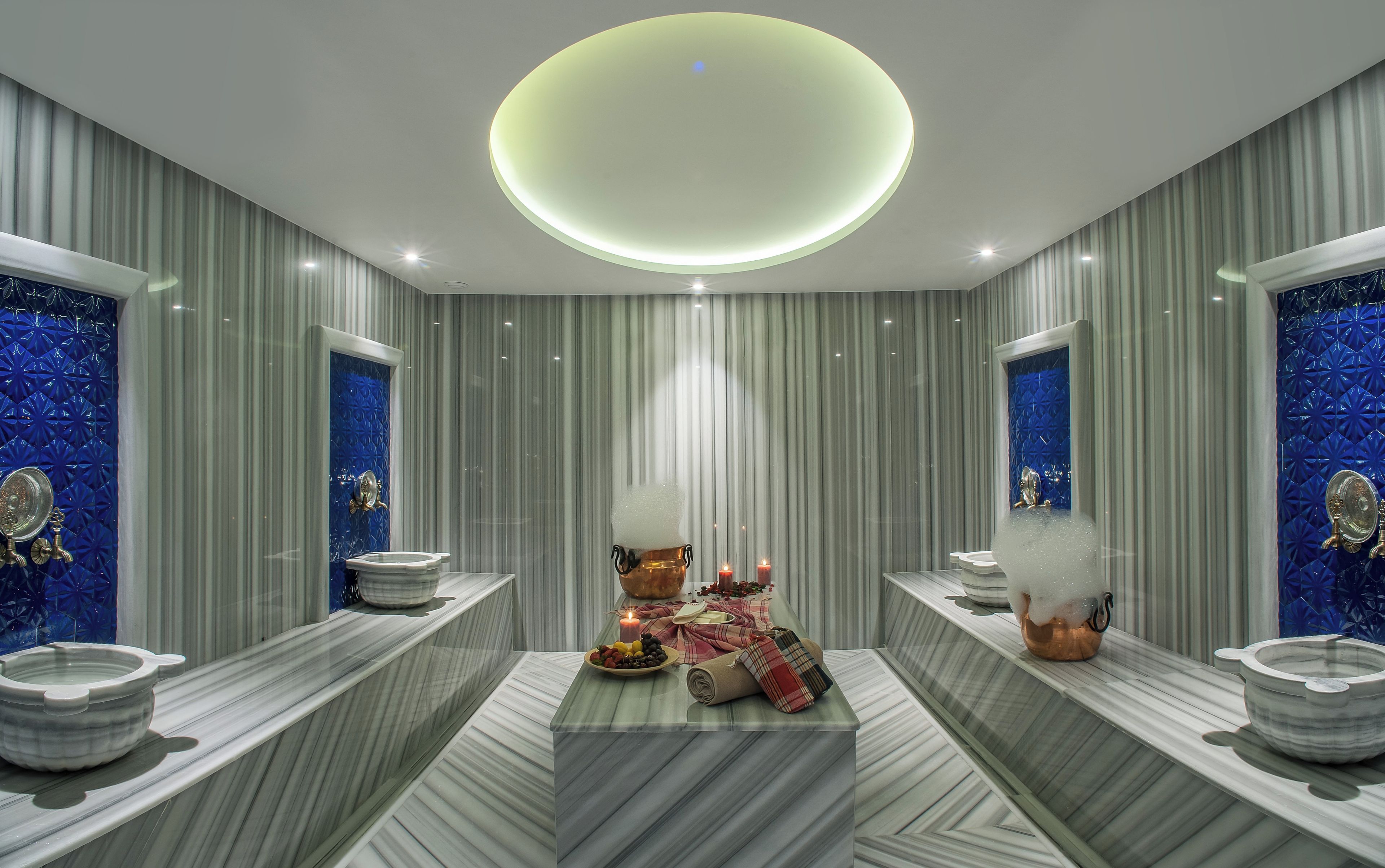 A modern bathroom with a central vanity, two sinks, a round mirror, and a unique ceiling light fixture.