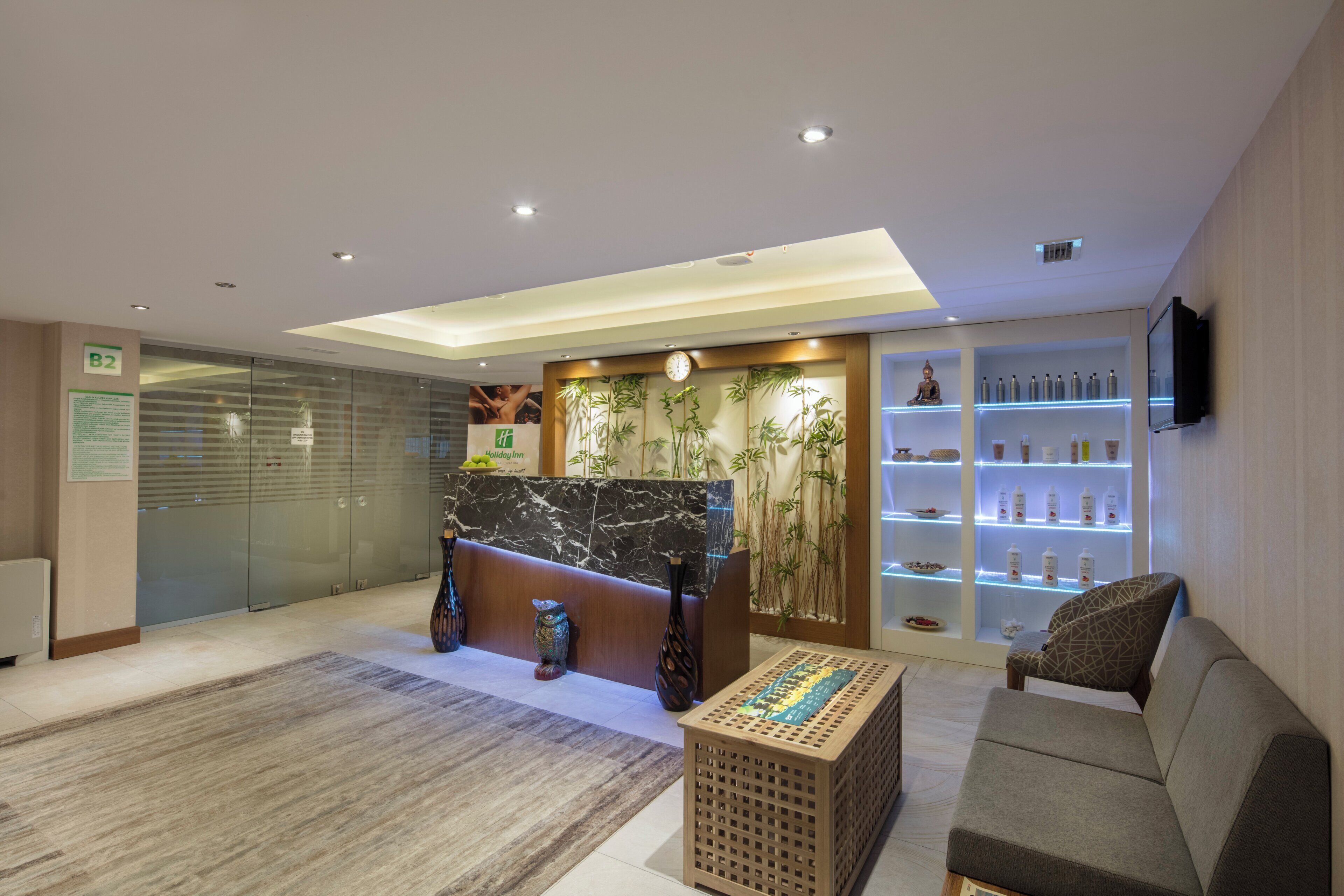 A hotel reception area with a marble counter, a sofa, a small table, and a shelf with toiletries.