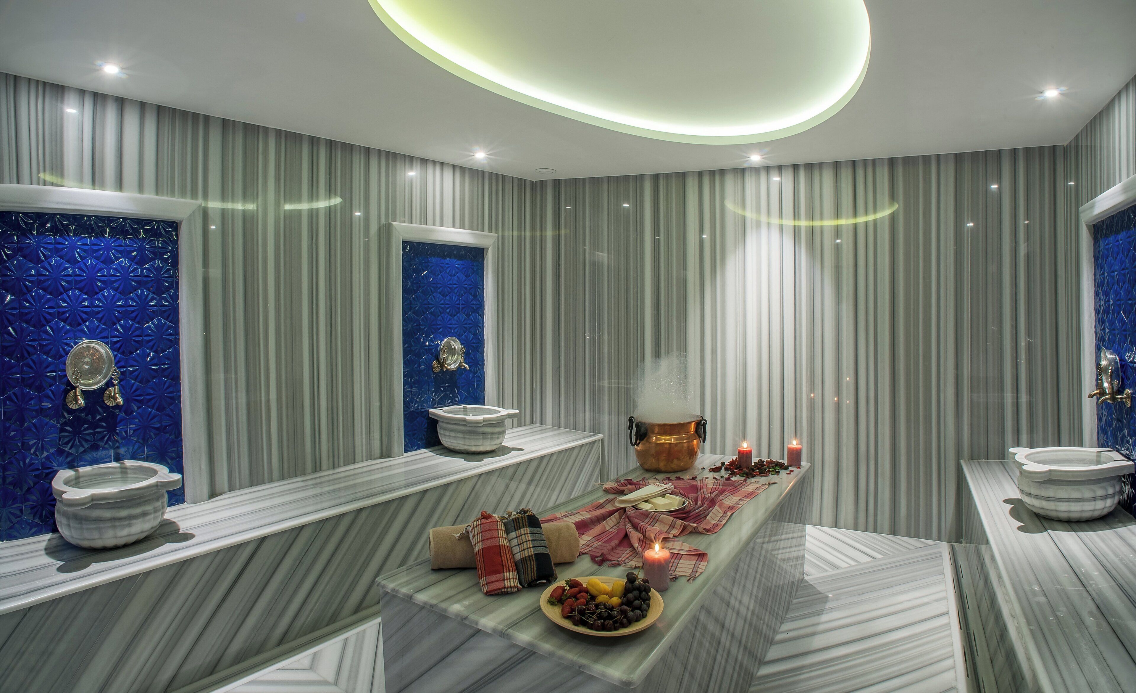 Un baño moderno con tocador de mármol, pared decorativa azul y una mesa central con velas y fruta.