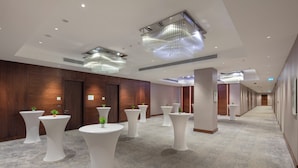Un couloir d’hôtel avec des tables rondes blanches, des panneaux de bois et des luminaires modernes.