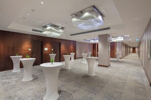 Un couloir d’hôtel avec des tables rondes blanches, des panneaux de bois et des luminaires modernes.
