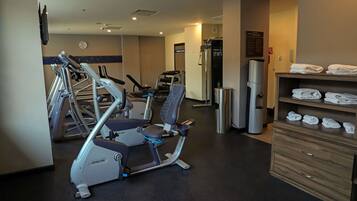 Un gimnasio de hotel con máquinas de cardio, equipo de pesas y un perchero para toallas.