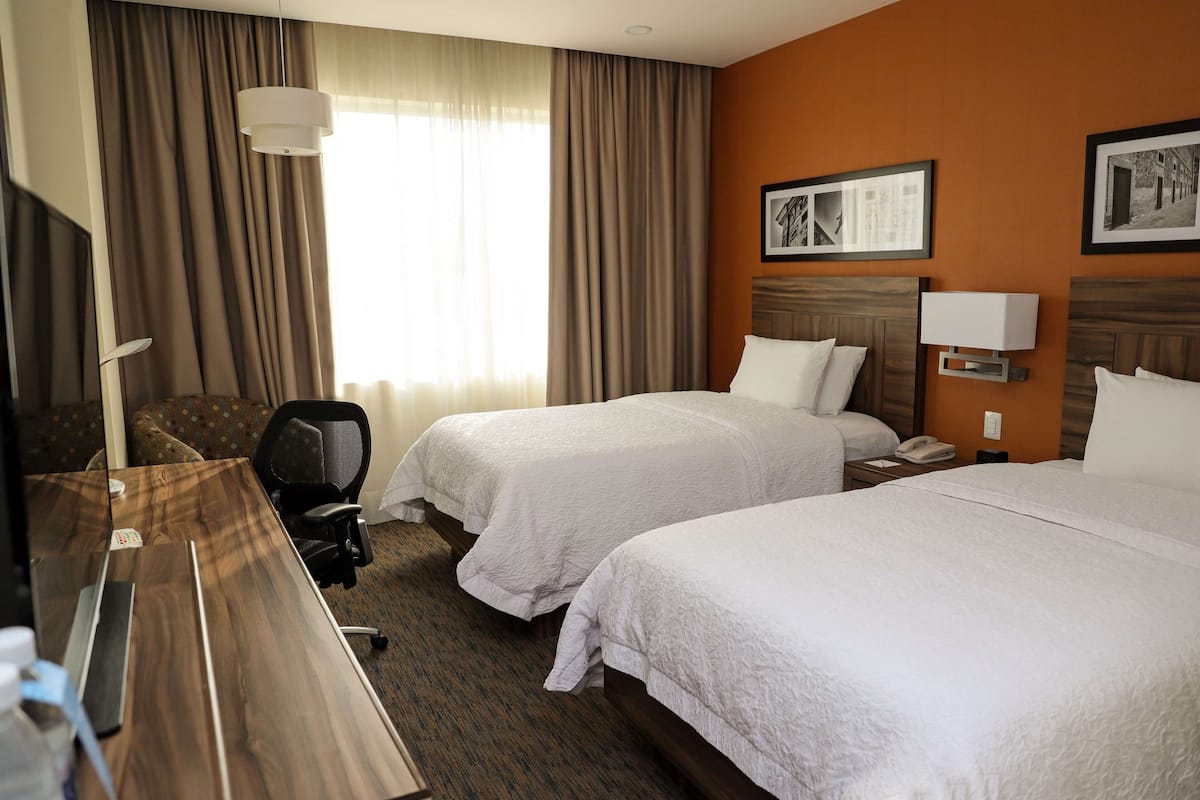 Habitación de hotel con dos camas, un escritorio, una silla y un televisor.