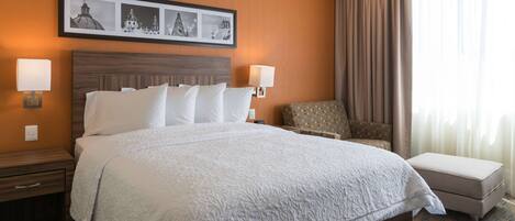 A hotel room with a large bed, two bedside tables, a chair, and a window with curtains.