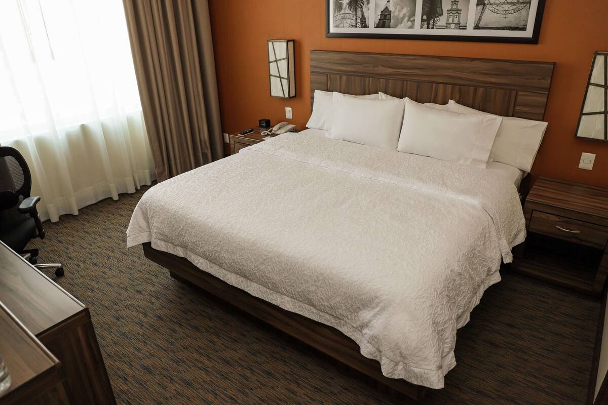 Habitación de hotel con una cama grande, cabecera de madera, mesita de noche con teléfono y escritorio con silla.