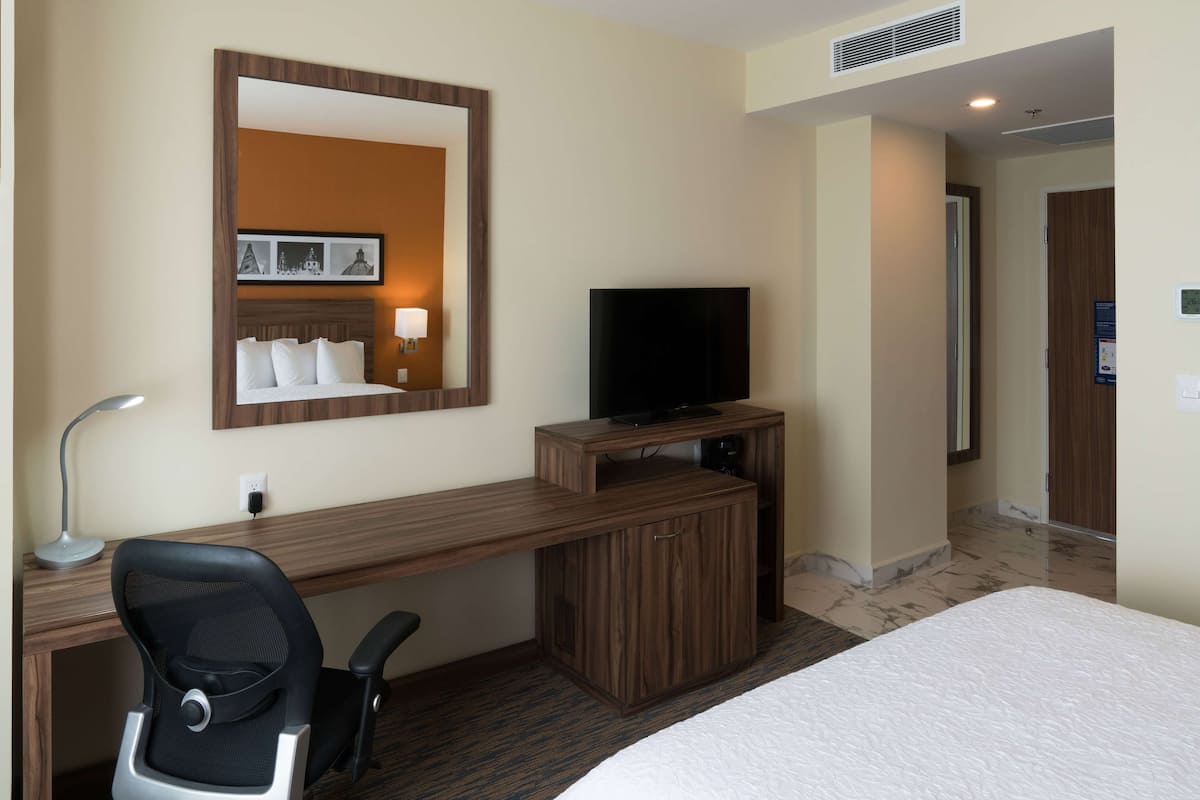 Una habitación de hotel con un escritorio de madera, televisor, cama y espejo.