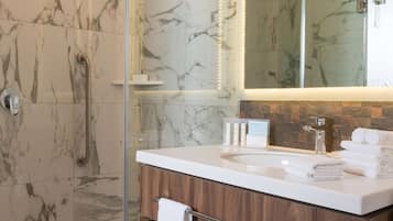 A modern bathroom with a glass-enclosed shower, marble walls, a wooden vanity, and a large mirror.